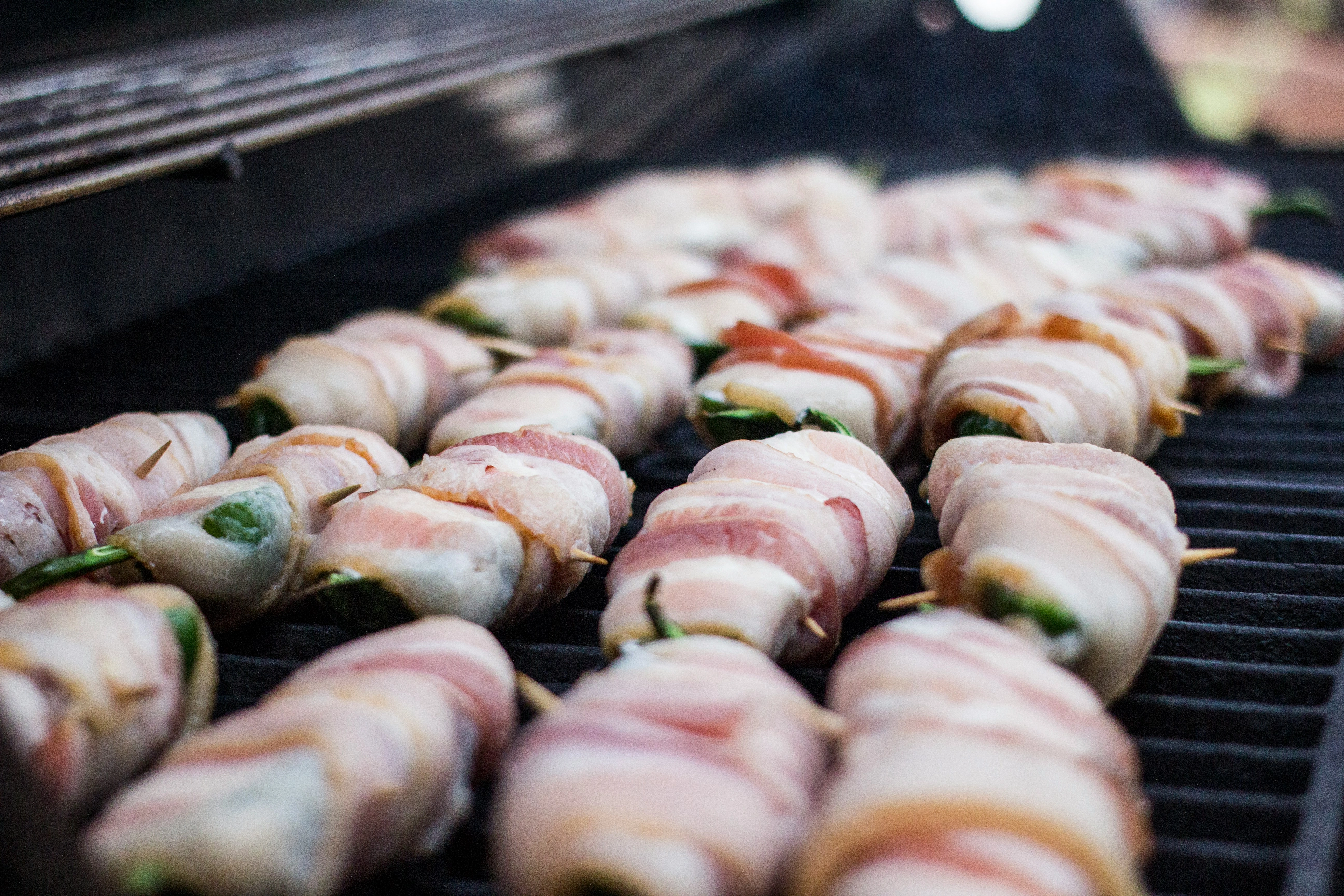 Jalapeno Poppers cooking on a propane grill. Bacon wrapped, cream cheese stuffed jalapenos are a must-have food for any cookout, BBQ or party.