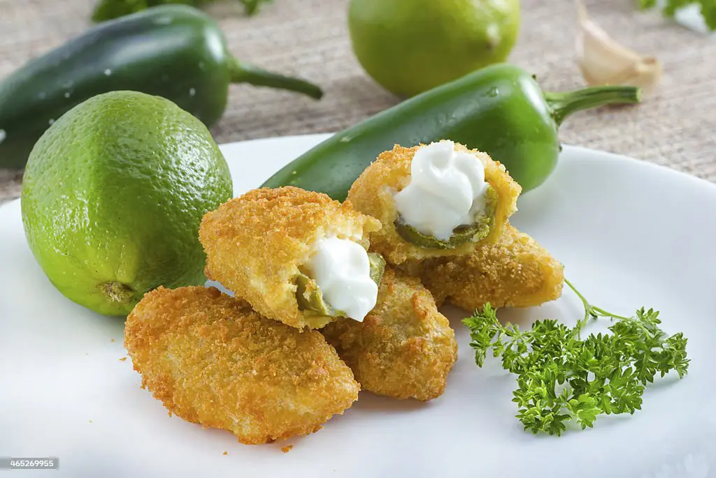 Cream chesse coming out of the jalapeno popper. with a lime and a whole jalapeno in the background of the picture.